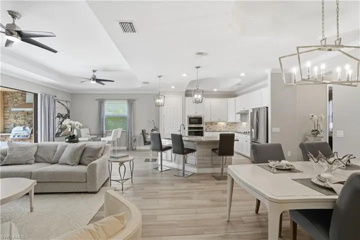 Living room featuring a tray ceiling, suspended lighting, light wood-style flooring, crown molding, and a ceiling fan