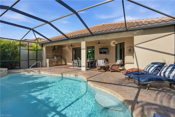 Outdoor pool with glass enclosure, an outdoor kitchen / dining area, a sunroom, and a patio