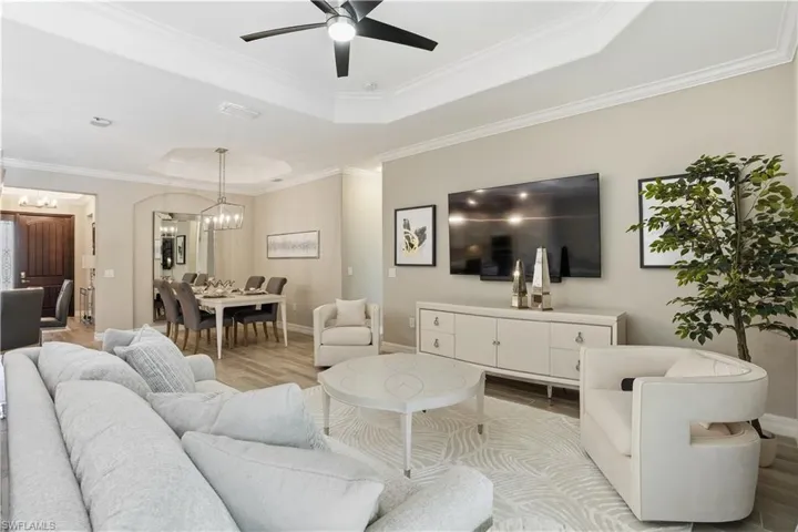 Living area with wood finished floors, ornamental molding, a raised ceiling, a ceiling fan, and hanging lights