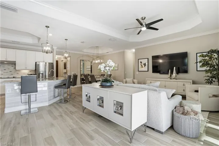 Living area with a raised ceiling, crown molding, a chandelier, wood finish floors, and ceiling fan