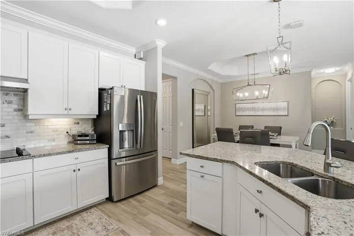 Kitchen with white cabinets, arched walkways, stainless steel fridge with ice dispenser, crown molding, and light stone counters
