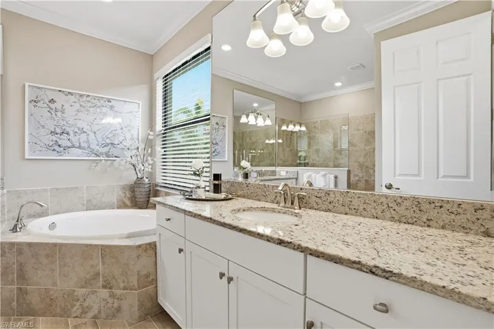 Bathroom with suspended lighting, vanity, walk in shower, a garden tub, and ornamental molding