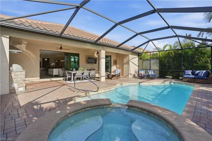 Relaxing pool / spa with a sunroom, a patio area, glass enclosure, and an outdoor kitchen / dining area