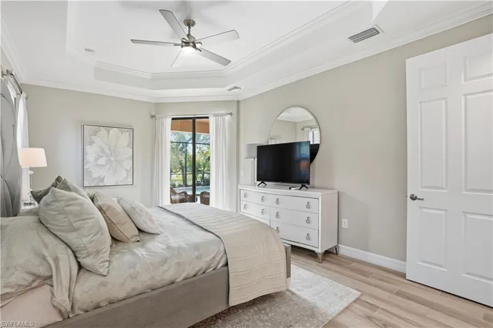 Bedroom with access to exterior, light wood finished floors, a raised ceiling, ornamental molding, and a ceiling fan