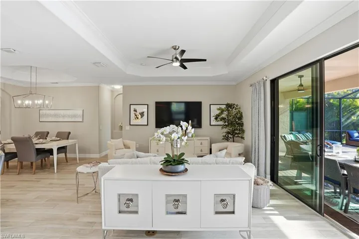 Living room with light wood-style floors, ceiling fan, crown molding, suspended lighting, and a tray ceiling