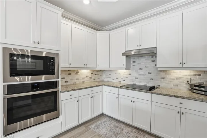 Kitchen featuring oven, white cabinets, built in microwave, light stone countertops, and ornamental molding