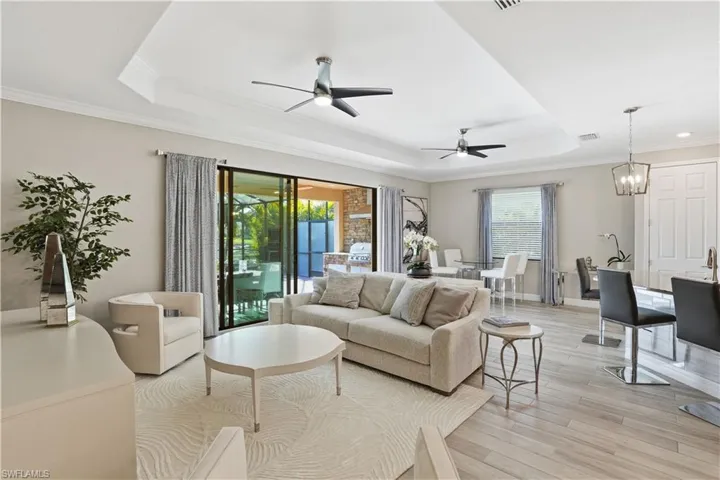 Living area featuring light wood-style floors, a tray ceiling, ceiling fan, crown molding, and a chandelier