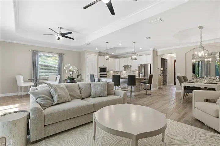 Living area featuring suspended lighting, a tray ceiling, light wood-style flooring, ornamental molding, and ceiling fan