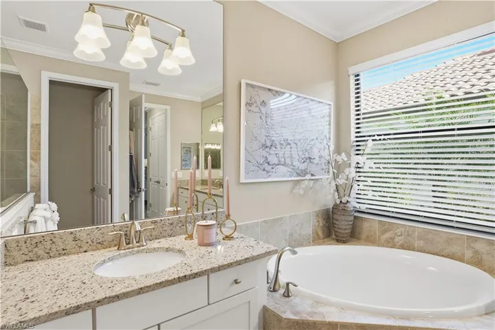 Full bath featuring crown molding, a bath, vanity, and hanging lights