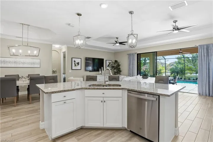 Kitchen featuring a ceiling fan, a tray ceiling, white cabinets, stainless steel dishwasher, and an island with sink