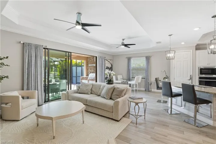 Living area featuring a raised ceiling, ornamental molding, light wood finished floors, a ceiling fan, and suspended lighting