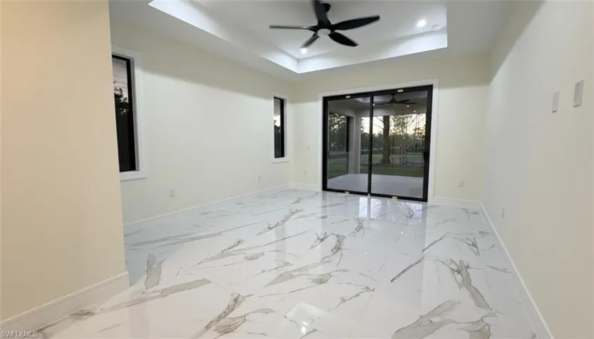 Empty room featuring a tray ceiling, light marble finish floors, and ceiling fan