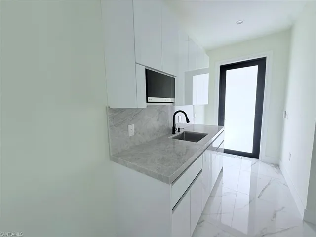Kitchen with modern cabinets, white cabinetry, light marble finish flooring, and backsplash