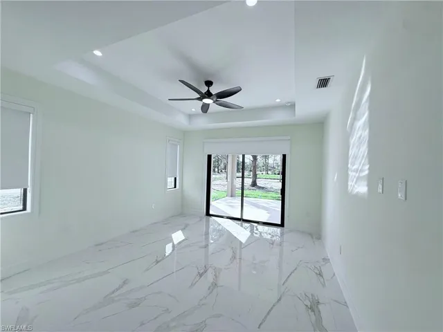 Empty room with light marble finish flooring, recessed lighting, a tray ceiling, and a ceiling fan