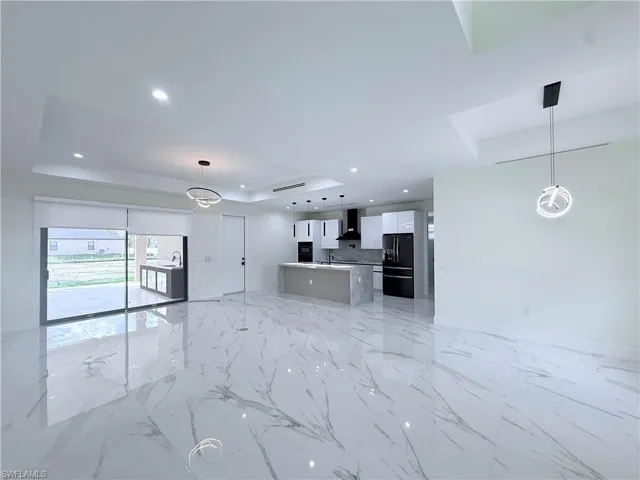 Kitchen with open floor plan, hanging light fixtures, a raised ceiling, black fridge with ice dispenser, and recessed lighting