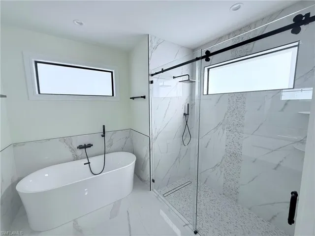 Full bath with a marble finish shower, a soaking tub, a wainscoted wall, marble finish floors, and healthy amount of natural light
