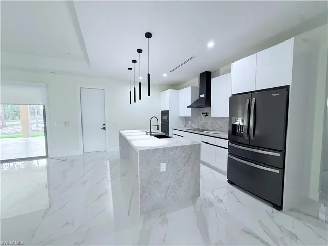 Kitchen featuring black appliances, pendant lighting, white cabinets, a kitchen island with sink, and wall chimney range hood