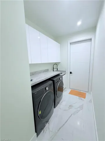 Laundry room featuring cabinet space, washer and clothes dryer, recessed lighting, and light marble finish flooring