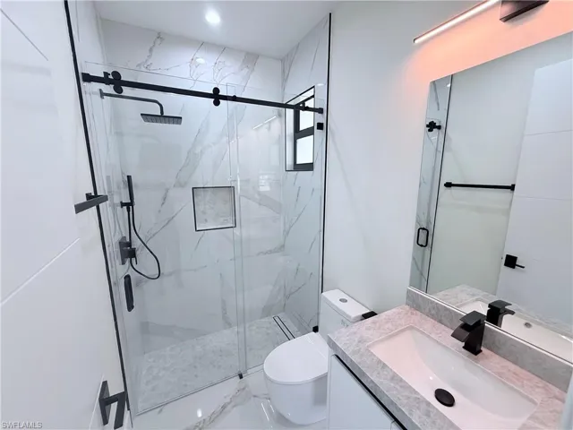 Full bath featuring vanity, a marble finish shower, and marble look tile flooring