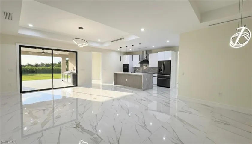 Unfurnished living room with a raised ceiling, light marble finish flooring, and recessed lighting
