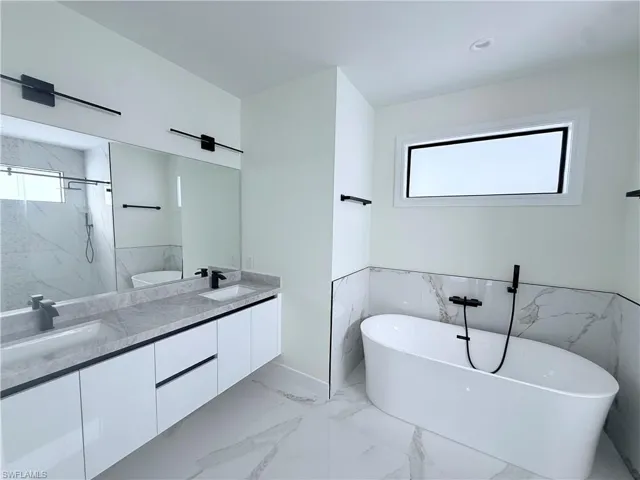 Bathroom with a freestanding bath, double vanity, a marble finish shower, light marble finish flooring, and a wainscoted wall