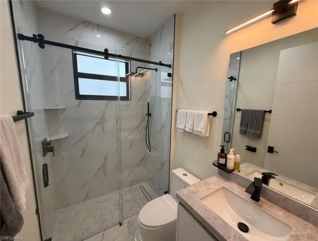 Full bath featuring vanity, a marble finish shower, and marble finish floors