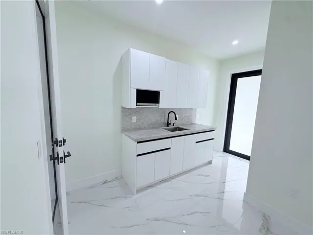 Kitchen featuring white cabinets, modern cabinets, backsplash, light stone countertops, and recessed lighting