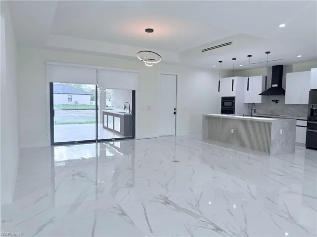 Kitchen with white cabinets, modern cabinets, hanging light fixtures, decorative backsplash, and wall chimney range hood