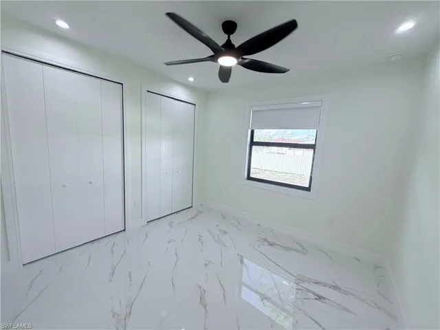 Unfurnished bedroom featuring multiple closets, light marble finish flooring, and ceiling fan