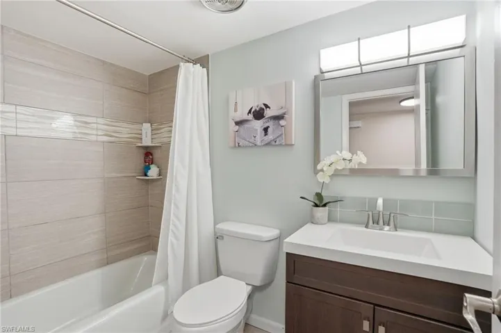 Bathroom featuring a tub/shower combination with light-toned horizontal tile, a floating vanity with an integrated sink, a rectangular mirror, and a contemporary light fixture