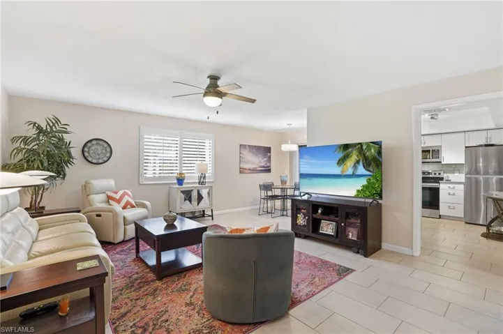 Living area featuring a ceiling fan, window with white louvered shutters, and tile flooring