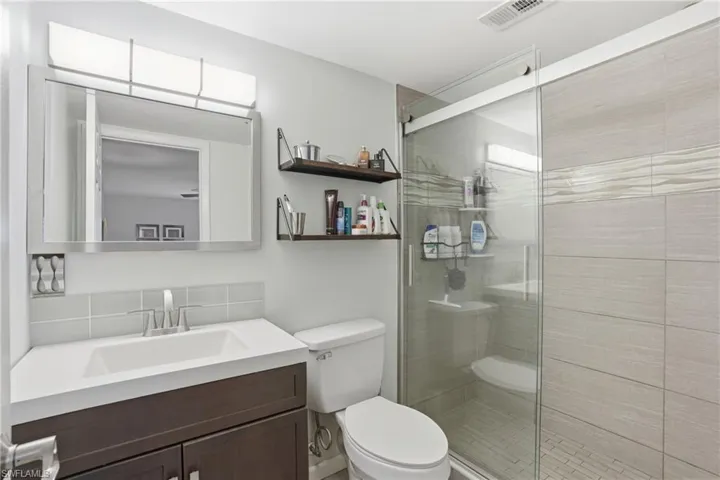 Contemporary bathroom featuring a dark wood-finish vanity with an integrated sink, a rectangular mirror, a sliding glass shower enclosure, a tiled shower interior with textured accent banding, and a white toilet
