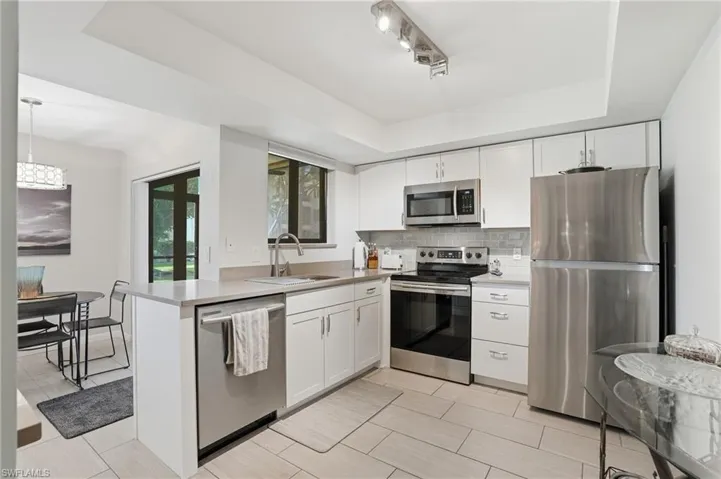 Modern kitchen featuring stainless steel appliances, white cabinetry, a light-toned countertop, a tile backsplash, and neutral tile flooring