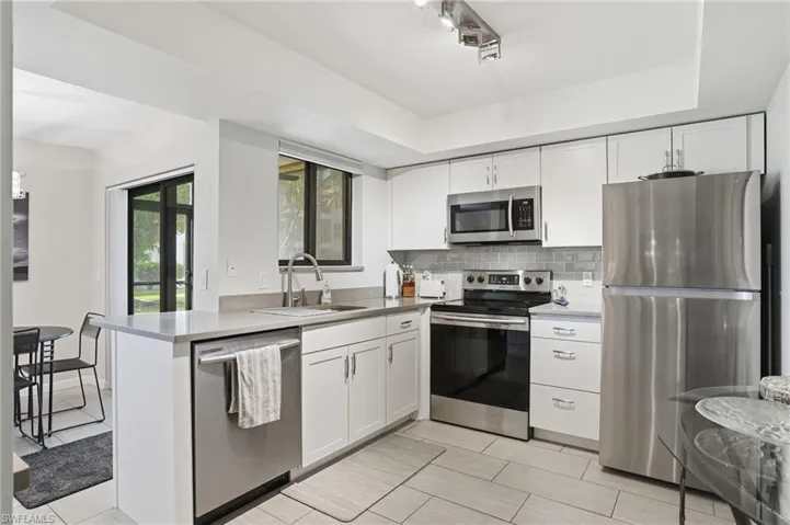Modern kitchen featuring stainless steel appliances, white cabinetry, light gray countertops, a subway tile backsplash, and light-toned tile flooring