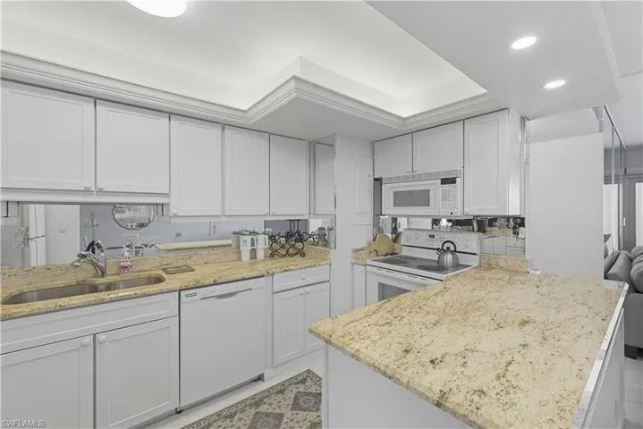 Kitchen featuring white appliances, white cabinetry, light stone counters, a peninsula, and recessed lighting