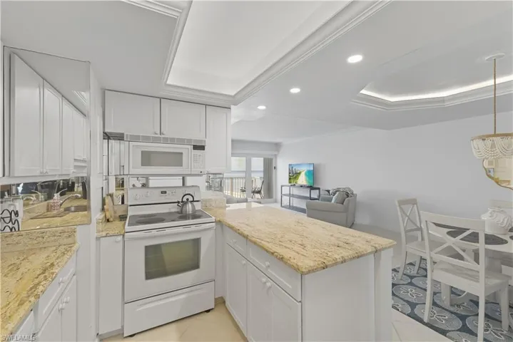 Kitchen featuring a raised ceiling, white appliances, a peninsula, white cabinetry, and recessed lighting