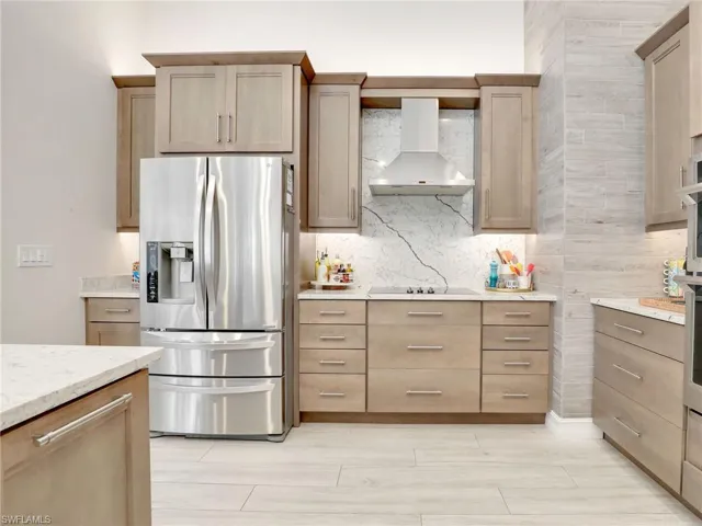 Kitchen with quartz counters & backsplash, stainless steel refrigerator, hood & gas cooktop