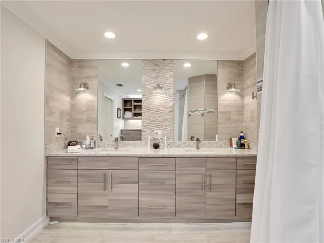 Primary bathroom w/ dual vanities, quartz counters, & stone and tile backsplash wall