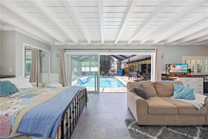 Bedroom with a wainscoted wall, access to outside, beamed ceiling, and stone tile flooring