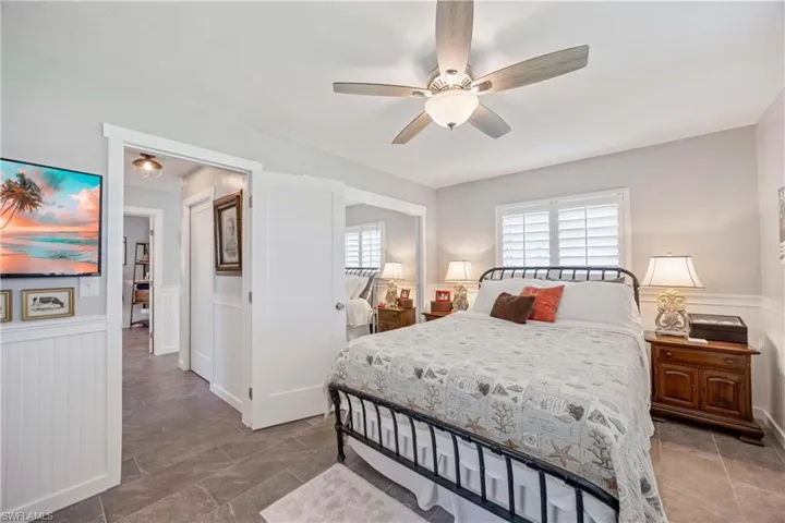 Bedroom featuring ceiling fan, wainscoting, and a decorative wall