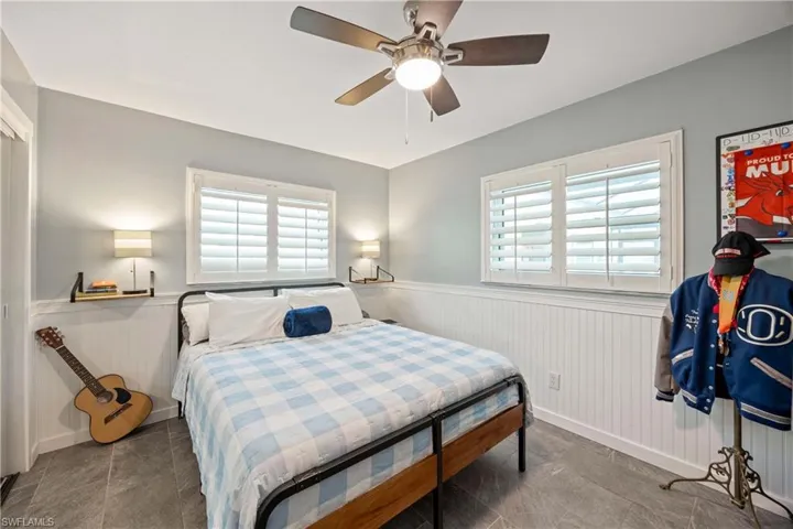 Bedroom with a wainscoted wall, multiple windows, baseboards, and a ceiling fan