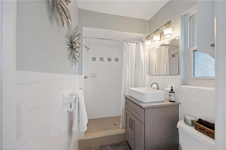 Full bath with a tile shower, toilet, and tile walls
