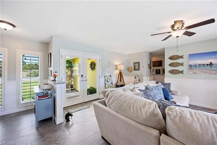 Living room featuring a ceiling fan, wainscoting, french doors, and tile patterned flooring