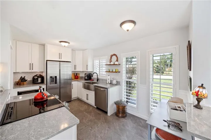 Kitchen with appliances with stainless steel finishes, tasteful backsplash, open shelves, a sink, and white cabinets