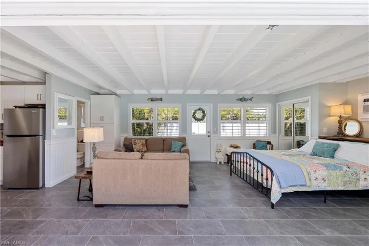 Bedroom with multiple windows, freestanding refrigerator, and beam ceiling