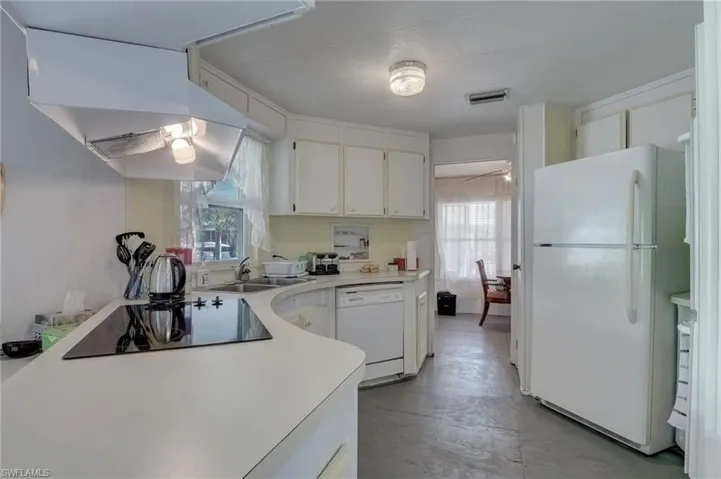 Kitchen with white cabinets, white appliances, light countertops, and concrete floors