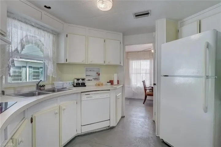 Kitchen featuring white appliances, white cabinetry, finished concrete floors, and light countertops