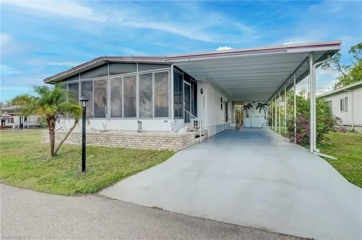 View of side of home featuring a carport, a sunroom, a yard, concrete driveway, and a patio area