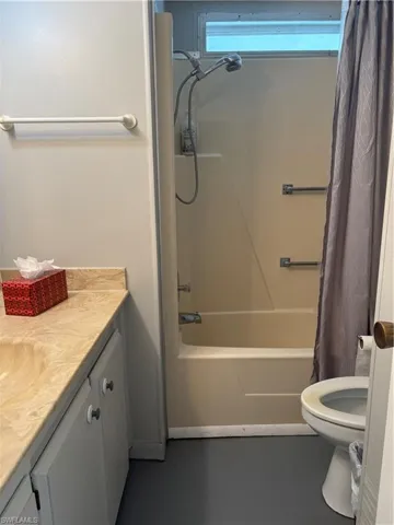Bathroom featuring a combined shower and tub unit, a single vanity with a solid surface countertop and white cabinetry, and gray flooring