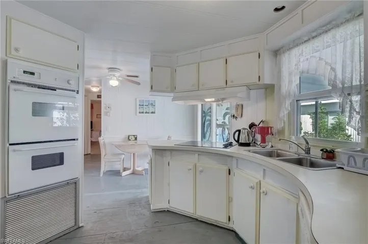 Kitchen with white double oven, light countertops, white cabinetry and a ceiling fan